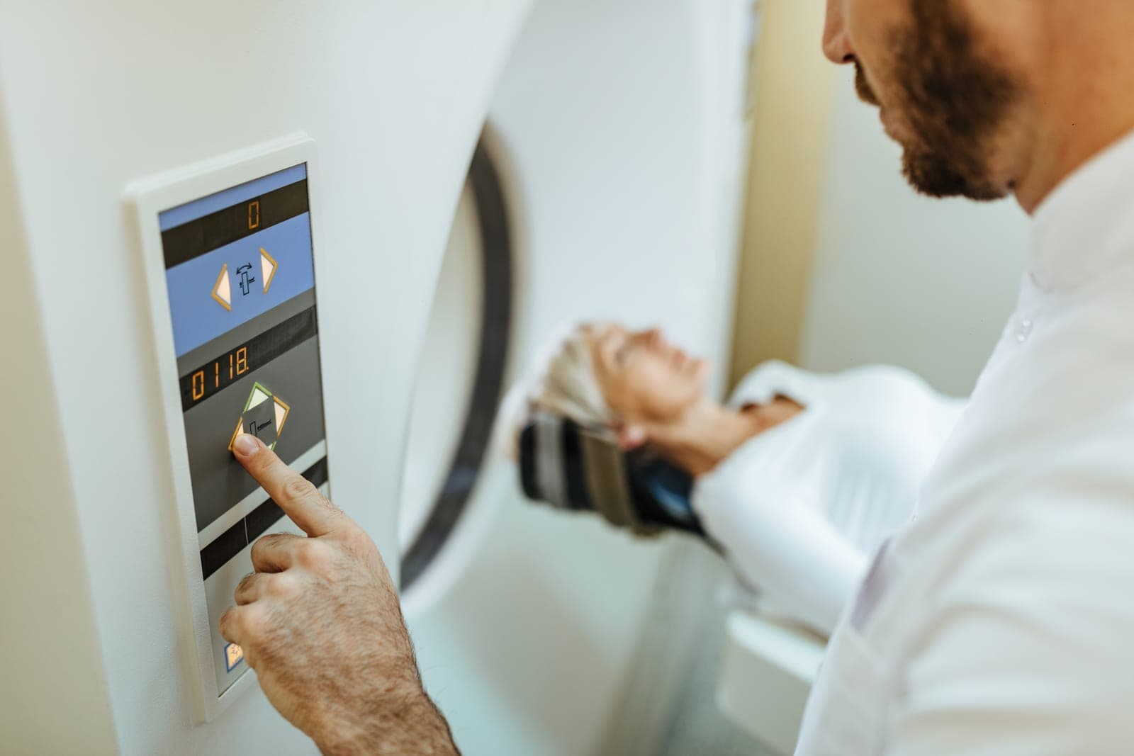 Profissional de saúde operando o equipamento de tomografia computadorizada enquanto paciente é posicionado para o exame