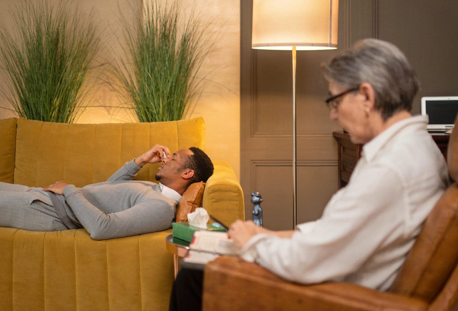 Paciente em sessão de psicoterapia deitado no divã enquanto terapeuta faz anotações