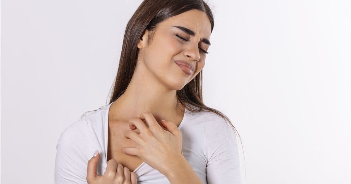 Mulher coçando o pescoço e o colo, região comum de dermatite de contato por colares e perfumes