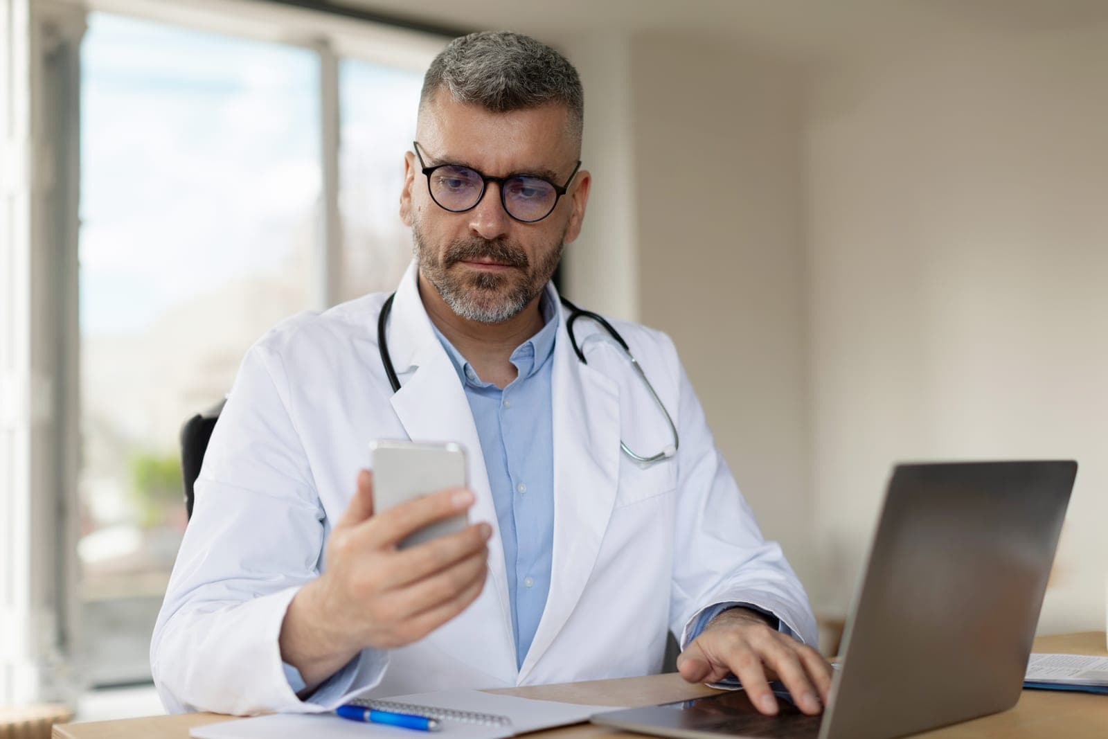 Médico avaliando paciente por teleconsulta a partir do celular e do laptop