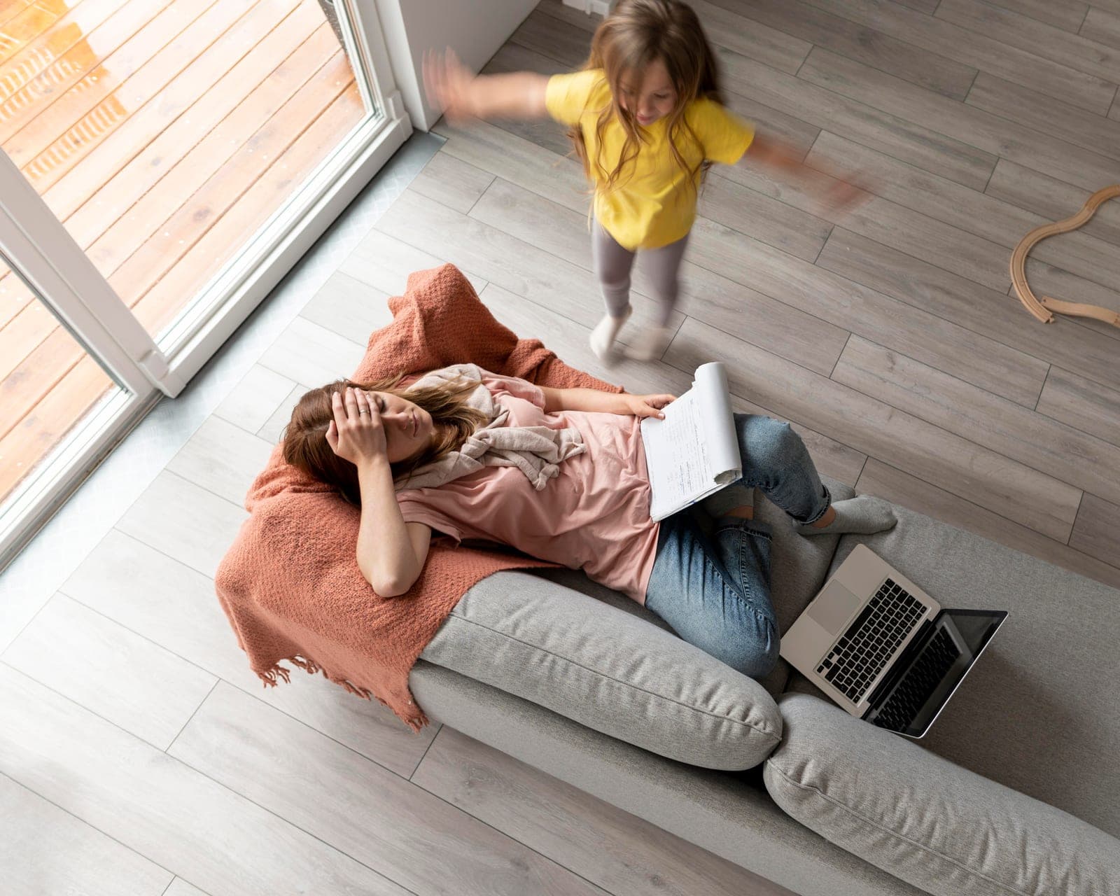Mãe tentando trabalhar em casa enquanto a criança corre agitada pelo ambiente