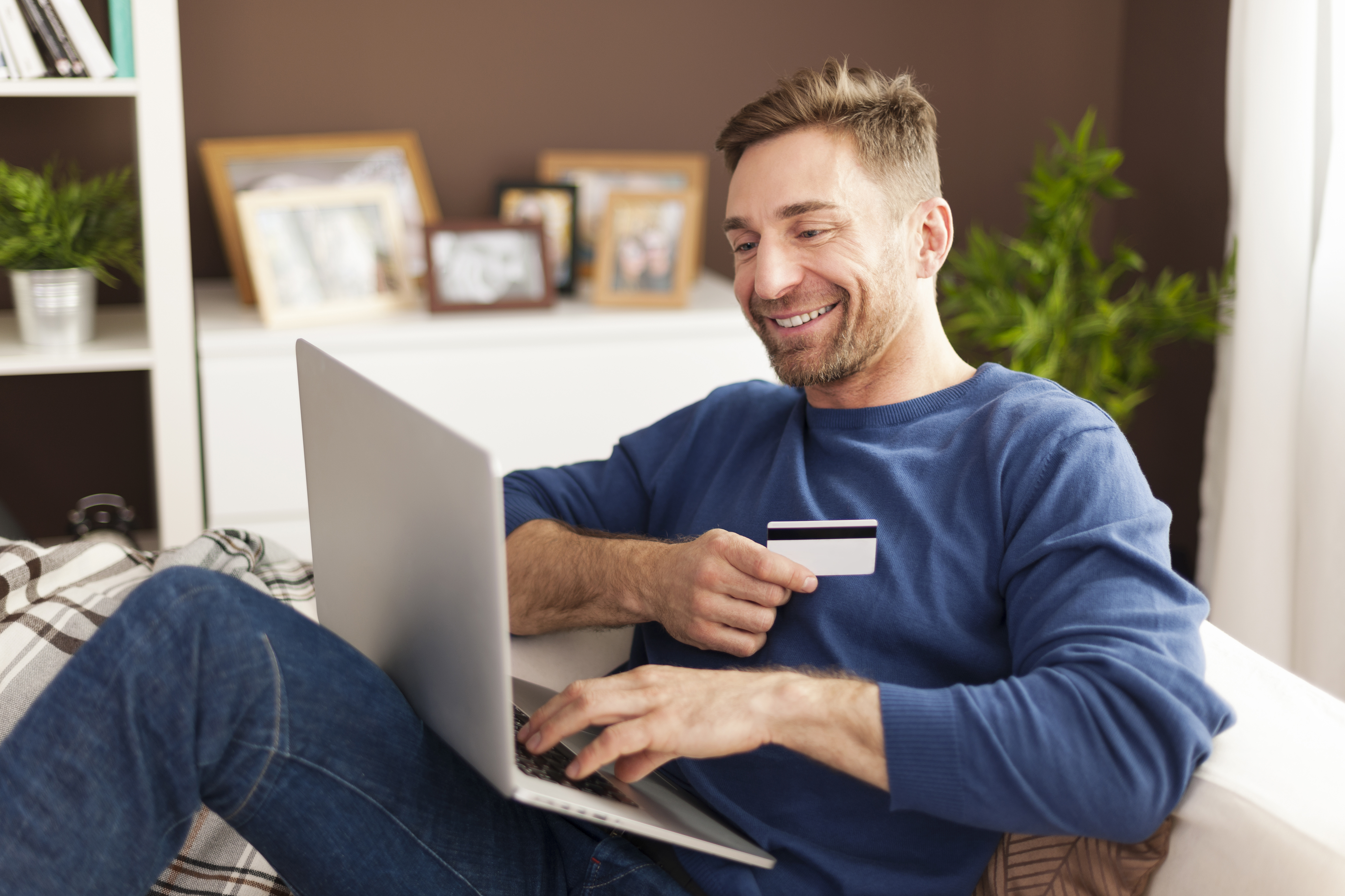 Homem no sofá com laptop e cartão de crédito realizando compra online