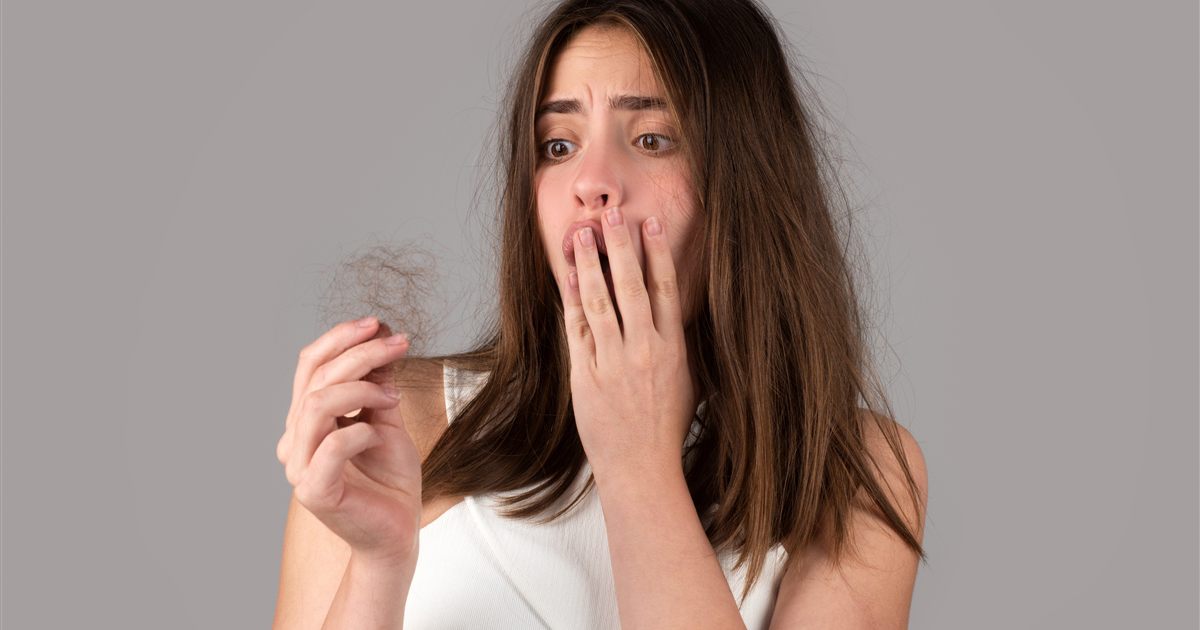 Mulher observando fios de cabelo na mão, avaliando a intensidade da queda